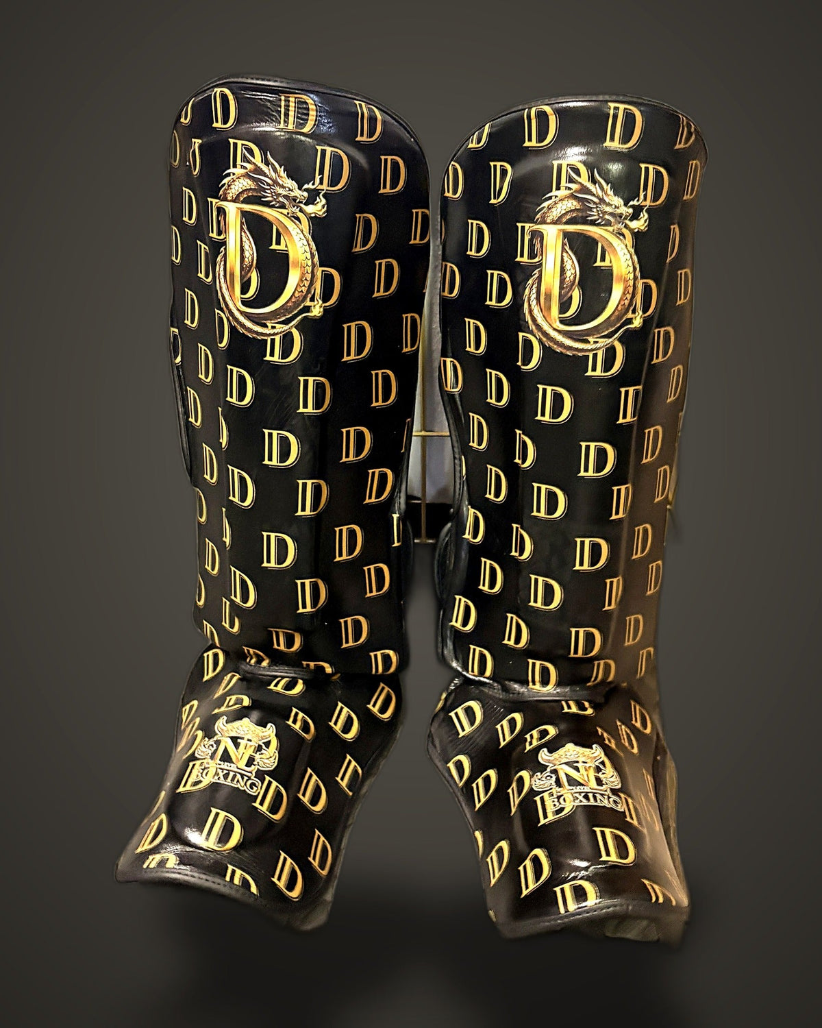 Dragon Monogram sponsorship shin guards — gold D monogram print with dragon crest, front view, New Level Boxing